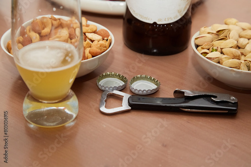 Bottle opener; beer glass with unfinished beer; bowls of nuts on the table close-up; beer snacks; atmosphere of a beer bar