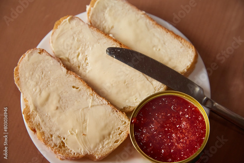 Three toasts with butter lie on a plate next to a jar of strawberry jam and a knife, toasts for breakfast, jam and toasts with butter on a plate, homemade breakfast with toasts