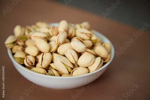 A plate of pistachios stands on a wooden table, pistachios in a plate, a plate of salted pistachios