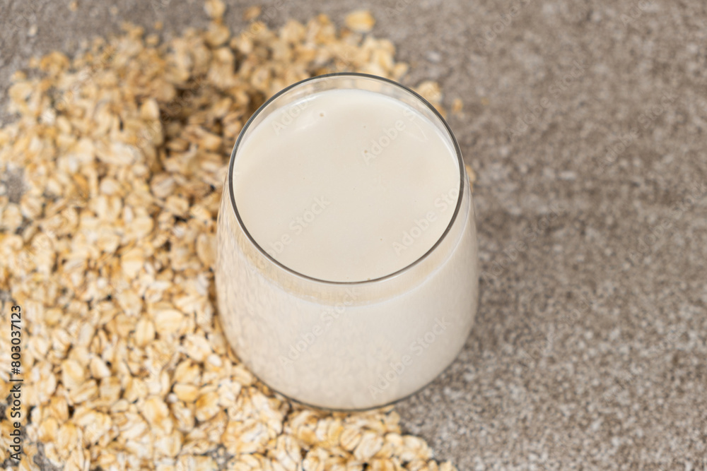Oat milk in a glass among dry oatmeal flakes on a gray background. Oat milk in a glass among dry oatmeal flakes on a gray background.