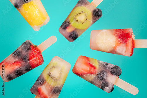 Popsicles filled with fresh fruit and lemonade float on a bright teal background