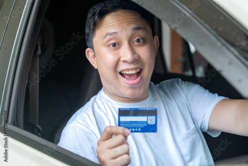 Adult Asian man smiling from inside his car while holding card or e-money. photo