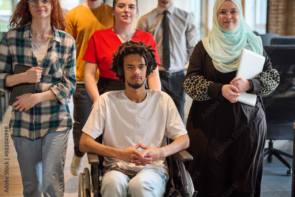 A diverse group of young business people congregates within a modern startup's glass-enclosed office, featuring inclusivity with a person in a wheelchair, an African American young man, and a hijab