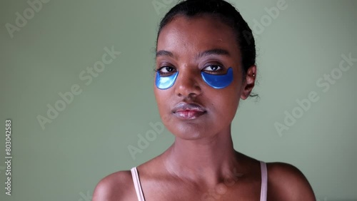 A black African American woman wearing sleeveless top is touching her under eye patches making sure it's properly place photo