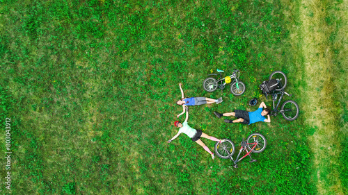 Family cycling on bikes aerial drone view from above, happy active parents with child have fun and relax on grass with bicycles, family sport and fitness outdoors
