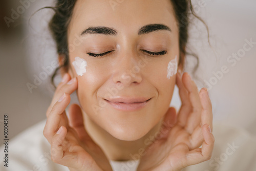 Young woman 30 years old applying face cream on her skin.