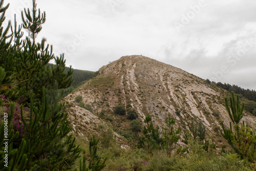 a rocky hill with erosion patterns, surrounded by greenery under a cloudy sky, highlighting nature's transformation photo