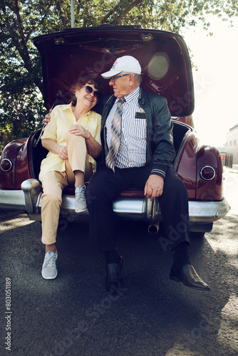 elderly husband and wife are sitting in the trunk of an old car holding hands © Alex