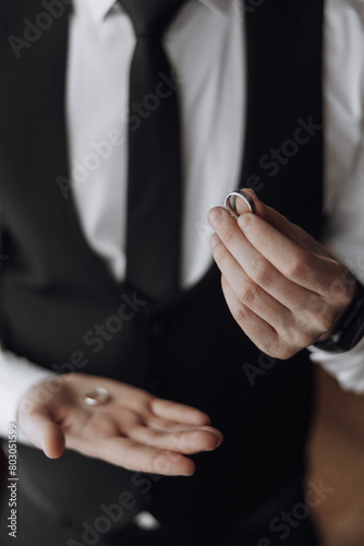 A man in a suit holding a ring in his hand. The man is wearing a black tie and a black vest