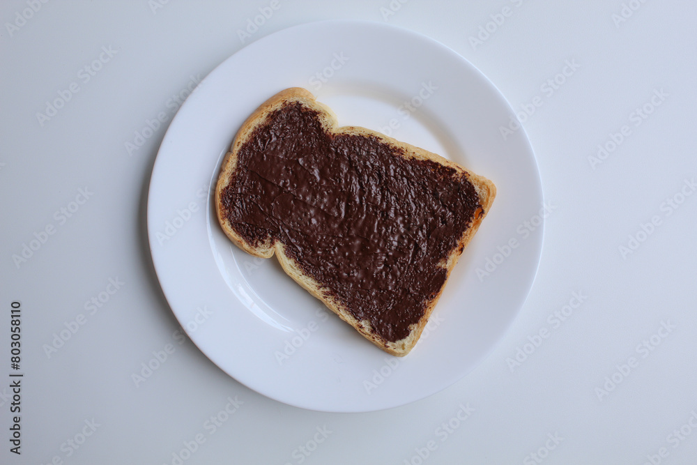 One slice of white bread, covered by chocolate spread, on white plate, isolated on white background. Prepare chocolate sandwich. Flat lay or top view One slice of white bread, covered by chocolate spread, on white plate, isolated on white background. Prepare chocolate sandwich. Flat lay or top view