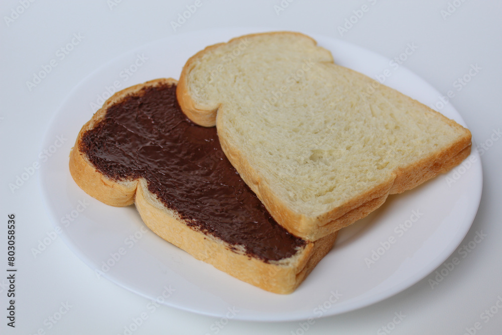 Two slices of white bread with chocolate spread or chocolate jam. Chocolate sandwich. On white plate, isolated on white background Two slices of white bread with chocolate spread or chocolate jam. Chocolate sandwich. On white plate, isolated on white background