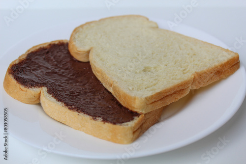 Two slices of white bread with chocolate spread or chocolate jam. Chocolate sandwich. On white plate, isolated on white background