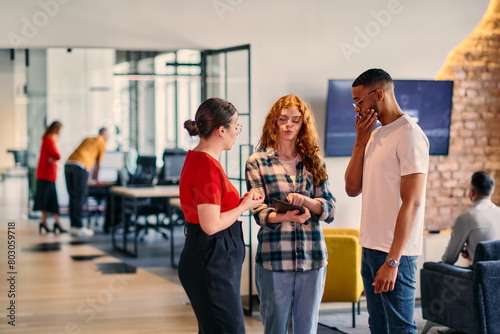 A group of young business individuals  including a girl with orange hair and an African American man  stands in a modern corporate hallway  collectively examining business progress on a smartphone