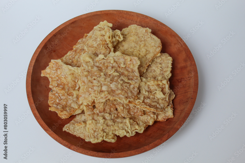 Keripik tempe or tempeh crackers, square shape. Thin slices tempeh, fried with flour dough. On wooden plate, isolated in white background Keripik tempe or tempeh crackers, square shape. Thin slices tempeh, fried with flour dough. On wooden plate, isolated in white background