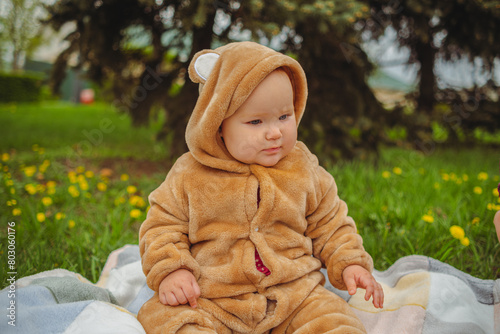 Baby in Bear Costume Sitting on Blanket. A baby wearing a bear costume sitting on a blanket in a cozy setting.