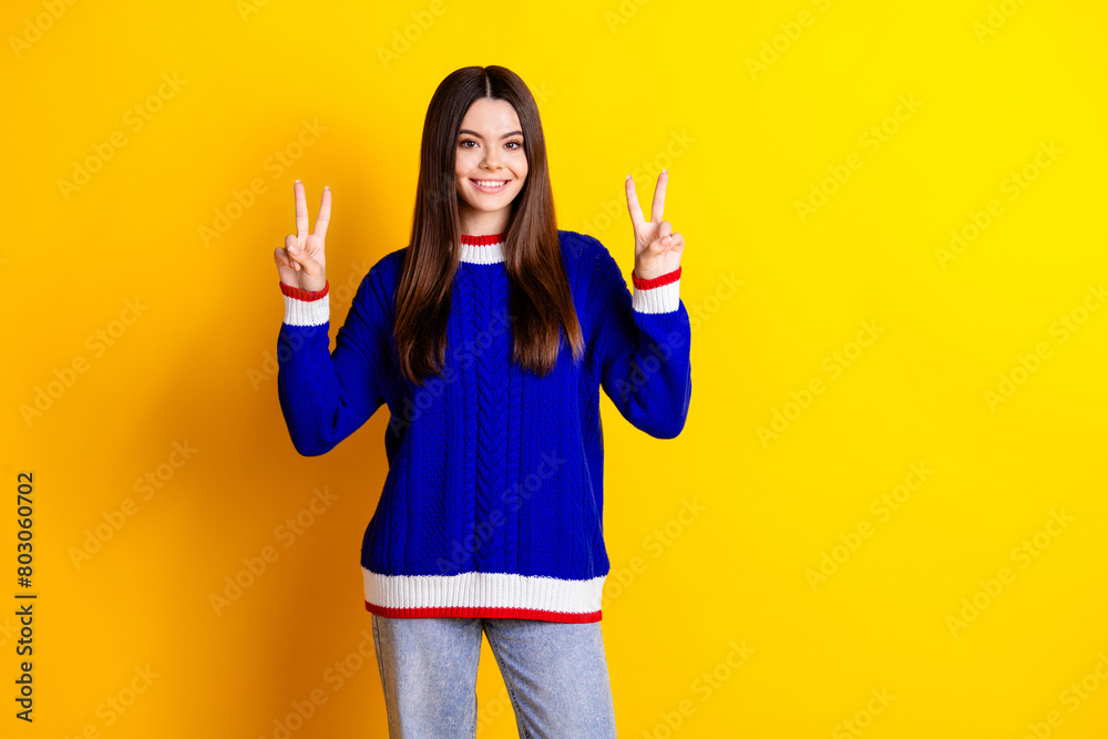 Photo portrait of pretty teen girl show v-sign wear trendy knitwear blue outfit isolated on yellow color background