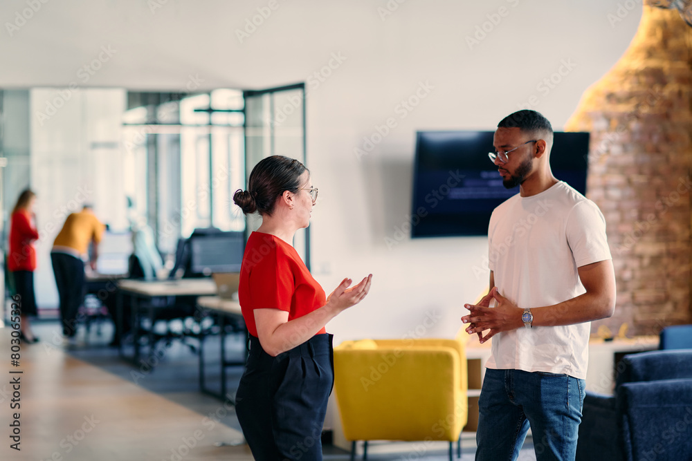 Obraz premium Young business colleagues, including an African American businessman, engage in a conversation about business issues in the hallway of a modern startup coworking center, exemplifying dynamic problem