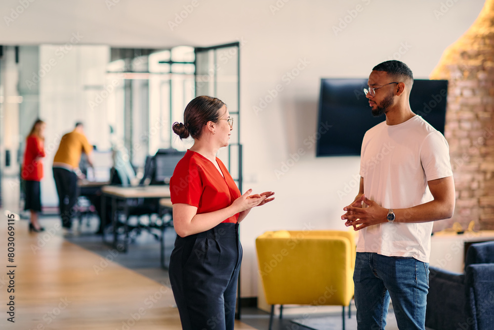 Obraz premium Young business colleagues, including an African American businessman, engage in a conversation about business issues in the hallway of a modern startup coworking center, exemplifying dynamic problem