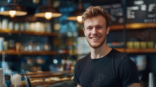 A confident man in a black t-shirt smiles warmly in a cafe, emanating casual professionalism.