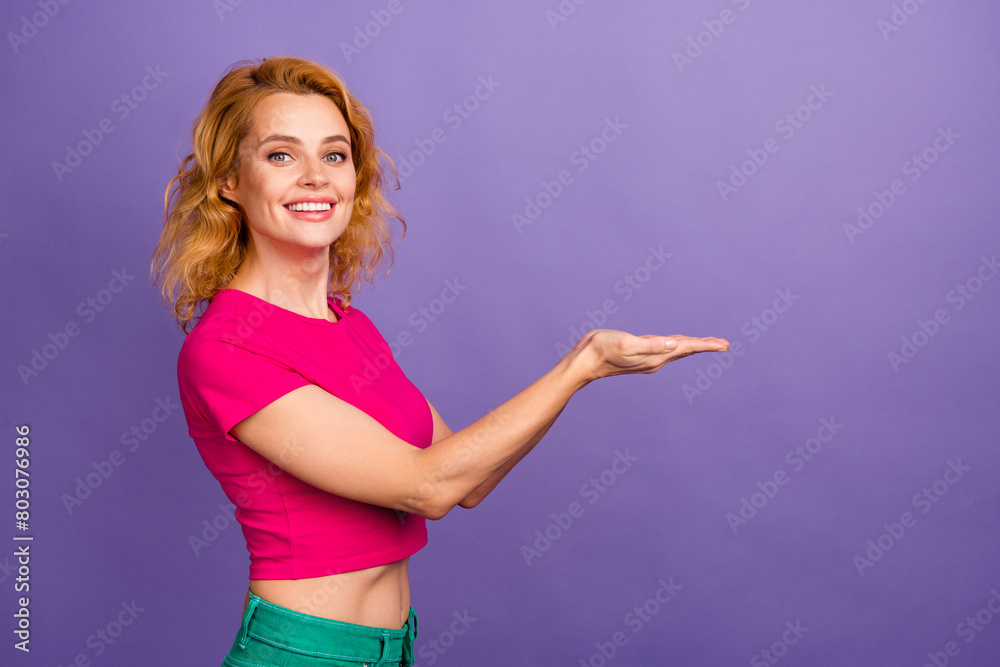 Profile side photo of lovely cute nice woman wear trendy pink clothes arms hold empty space isolated on purple color background Profile side photo of lovely cute nice woman wear trendy pink clothes arms hold empty space isolated on purple color background