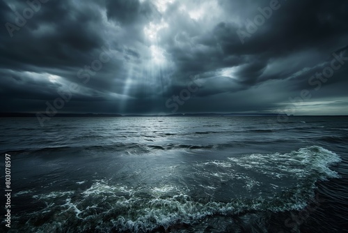 The image captures a moody and dramatic ocean scene with sunbeams breaking through heavy storm clouds, reflecting on the turbulent waves photo