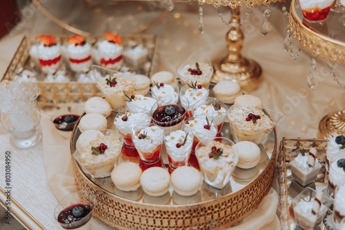 A table with a variety of desserts, including cakes, pastries, and fruit tarts. The desserts are arranged in small, individual serving dishes, and there are also some drinks on the table