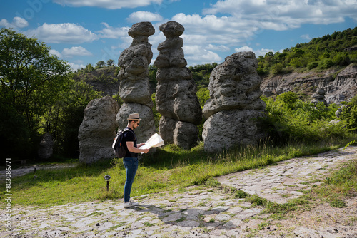 A young man explores new destinations by traveling through North Macedonia.He is standing next to stone figures and looking at a map.