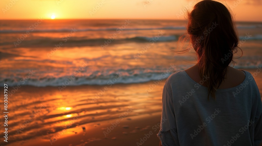 Woman watching sunset at the beach, a serene evening seascape.
