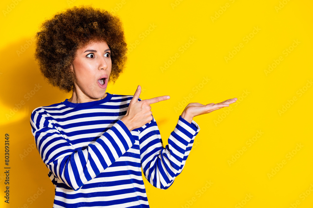 Photo of nice young girl direct finger arm hold empty space wear striped shirt isolated on yellow color background Photo of nice young girl direct finger arm hold empty space wear striped shirt isolated on yellow color background