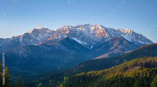 Sunrise over snow-capped mountain range with forested valley. Golden light on peaks.