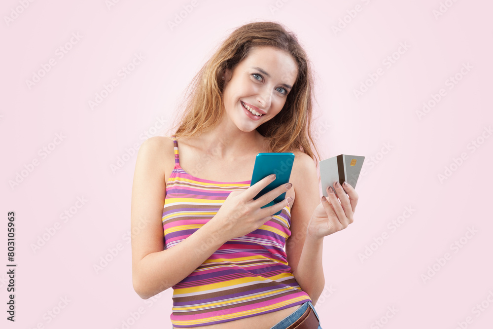 Happy and smiling young woman uses her mobile phone and credit card to browse an internet web page or online store, using her smartphone for shopping and online payments. Isolated on pink background