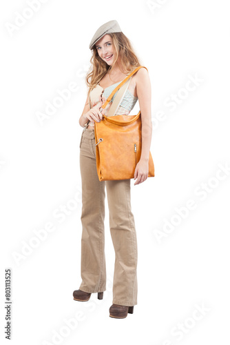 The smiling young woman, carrying a vintage leather bag, wears fashion stylish clothes and a hat while standing isolated against a white background, looking into the camera with her blue eyes © amedeoemaja