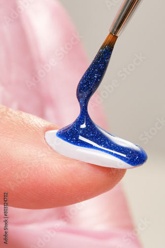 Close up process of applying blue pearlescent varnish. Blue glitter nail polish and brush, macro. Shallow depth of field