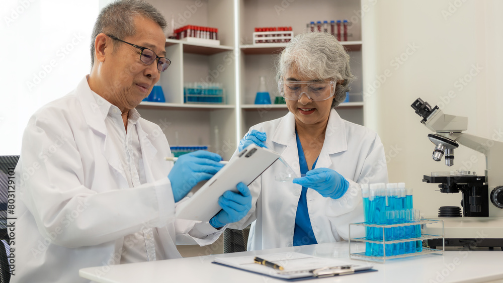 A team of 2 senior Asian scientists perform a thought experiment and a senior male leader prepares test tubes and analyzes a computer microscope in a laboratory. teamwork A team of 2 senior Asian scientists perform a thought experiment and a senior male leader prepares test tubes and analyzes a computer microscope in a laboratory. teamwork