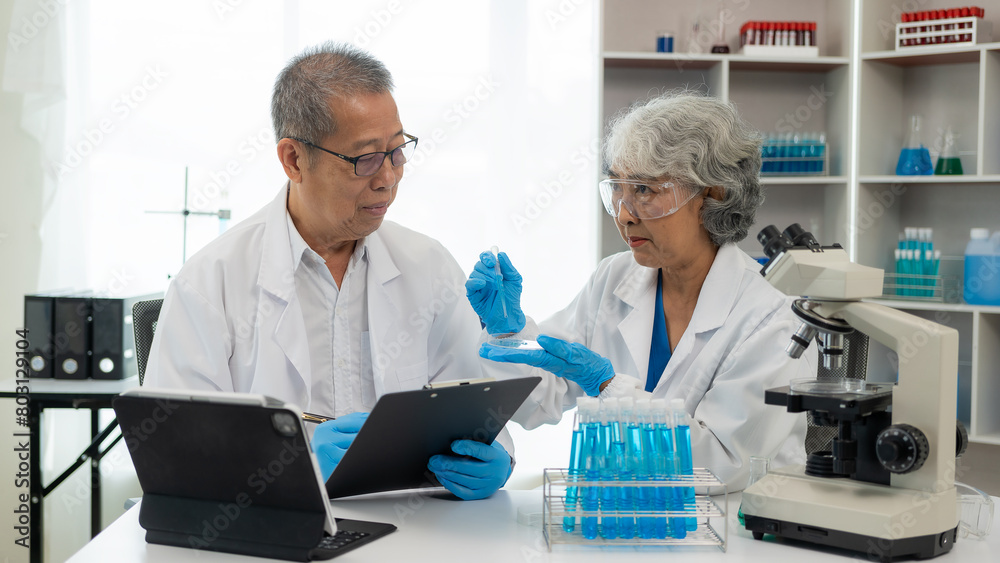 A team of 2 senior Asian scientists perform a thought experiment and a senior male leader prepares test tubes and analyzes a computer microscope in a laboratory. teamwork A team of 2 senior Asian scientists perform a thought experiment and a senior male leader prepares test tubes and analyzes a computer microscope in a laboratory. teamwork