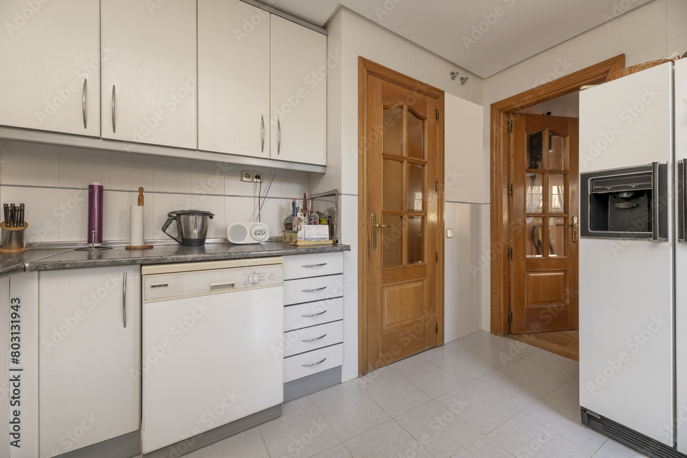 Fototapeta premium A kitchen with white cabinets, gray countertops, tiled backsplash and oak doors on two walls