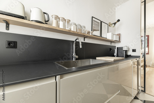 A modern kitchen with glossy lacquered wood furniture, black stone countertop and backsplash of the same material