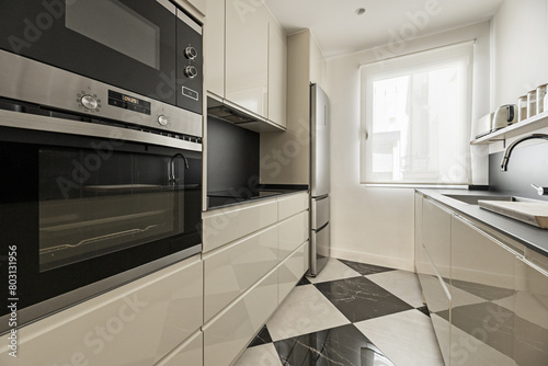 A modern kitchen with glossy lacquered wood furniture, black stone countertop, backsplash of the same material, checkered marble floors and integrated appliances