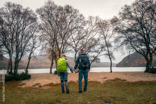 Amazing panoramic view with lake, beach, trees, valley and rocky steep mountain. Bad, foggy and depressing weather. Couple holding by hand,  enjoying lake view. © Marcin