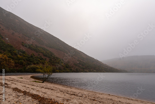 Beautiful panoramic view with lake, beach, trees, valley and rocky steep mountain. Bad Depressing weather. Lough Dan lake in Wicklow Mountains, Ireland