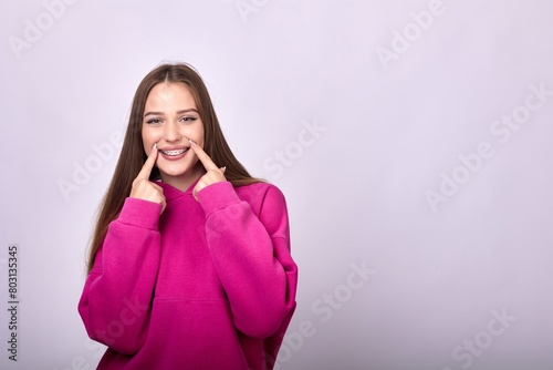An attractive toothy caucasian female in her 20s with long straight brown hair. Wearing a fashionable pink pullover hoodie sweatshirt. Isolated on a white background.