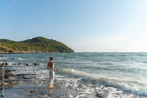 Lonely woman stand alone on the rock beach among wave of sea and sunshine to relax on vacation