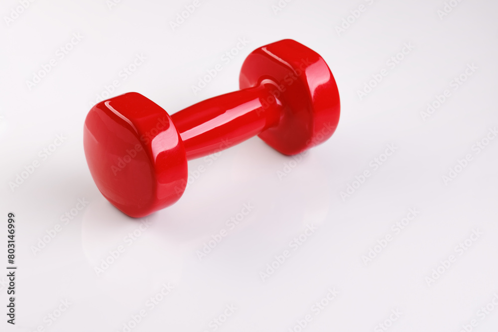 A red dumbbell lies on a white glass surface. There is both a shadow and a reflection at the same time. Selective focus. A red dumbbell lies on a white glass surface. There is both a shadow and a reflection at the same time. Selective focus.