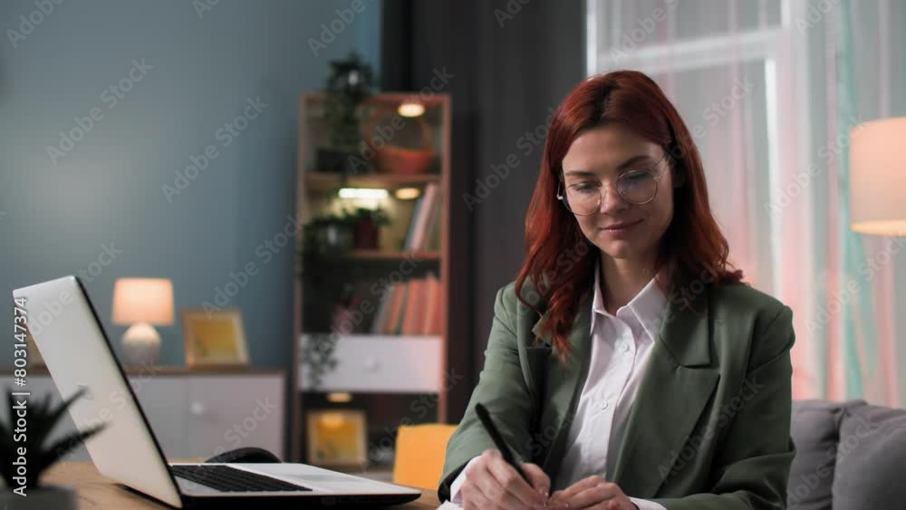remote work, female office employee working at a laptop making notes in a notepad while sitting in room remote work, female office employee working at a laptop making notes in a notepad while sitting in room