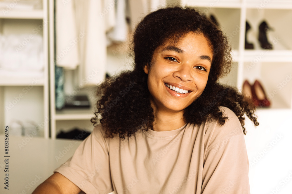 A close-up portrait of a young smiling teenage girl of mixed race in a home dressing room. A young charming African woman in a beige T-shirt is laughing in the living room. A close-up portrait of a young smiling teenage girl of mixed race in a home dressing room. A young charming African woman in a beige T-shirt is laughing in the living room.