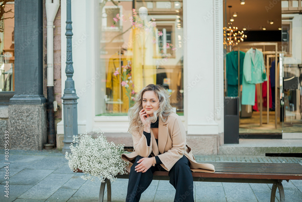 Portrait of beautiful young blonde woman with bouquet of white flowers in the center of European city. Happy model in casual spring clothes. Holiday. Portrait of beautiful young blonde woman with bouquet of white flowers in the center of European city. Happy model in casual spring clothes. Holiday.