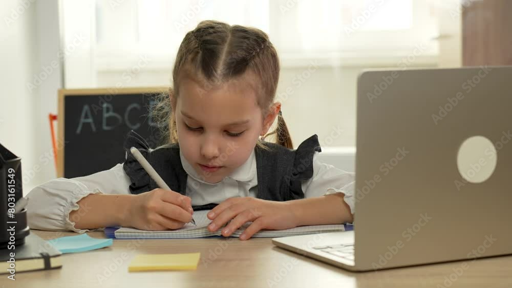 School girl using laptop sitting at desk writing notes while watching webinar, studying online School girl using laptop sitting at desk writing notes while watching webinar, studying online