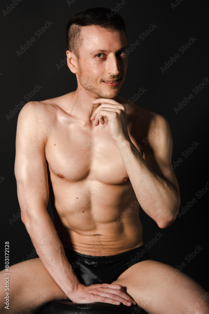 A man with a beautiful body poses in the studio against a black background.