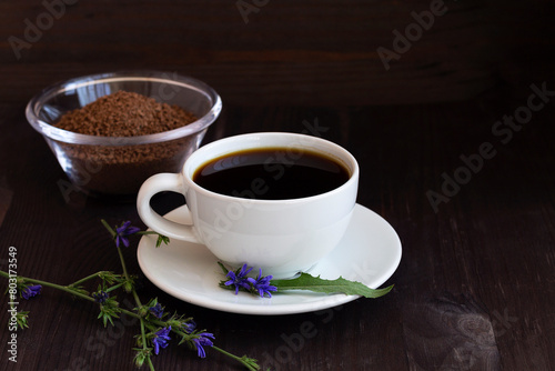 hot chicory drink in white cup with blue chicory flowers and Ground chicory root on dark brown wooden background. healthy. coffee substitute. copy space.