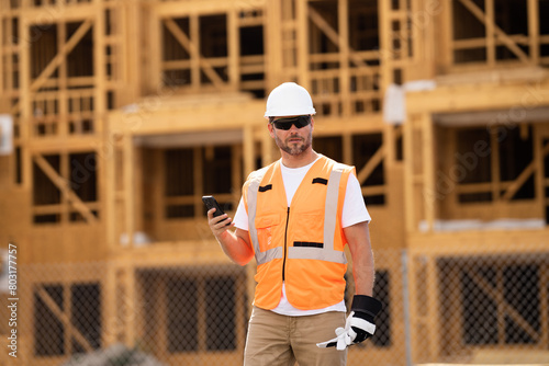 roofer builder working on roog structure of building on construction site. handsome young male builder in hard hat smiling at camera. Construction Worker on Duty. Contractor and the Wooden House Frame